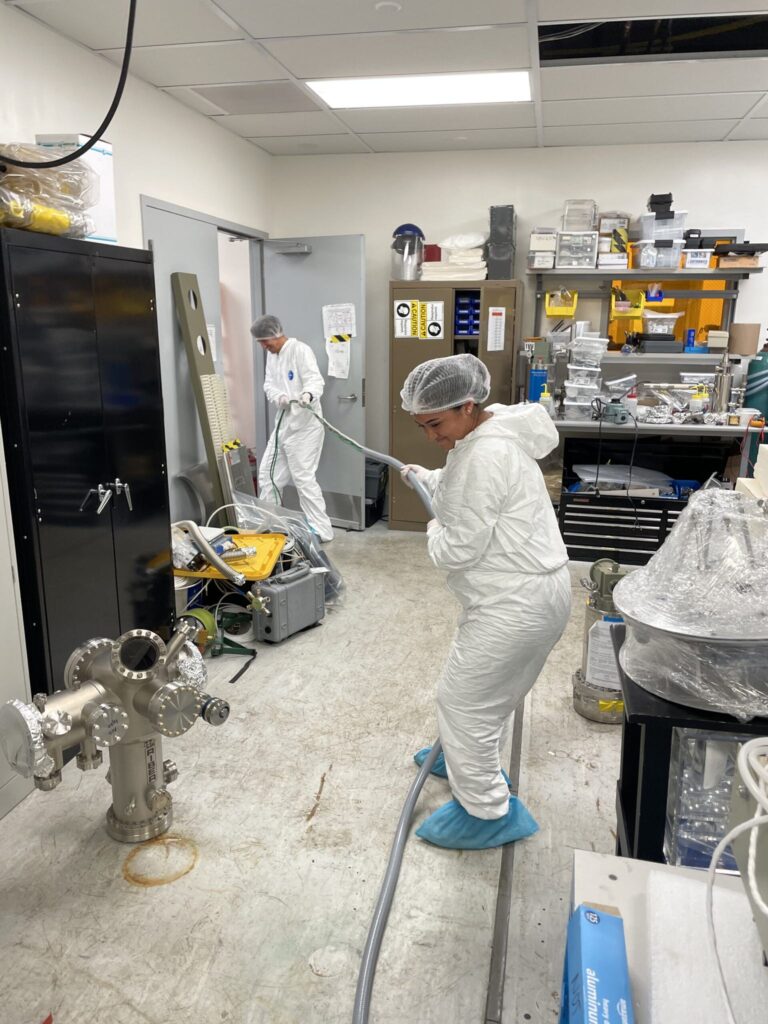 Lab members in cleanroom suits pulling cable through a doorway