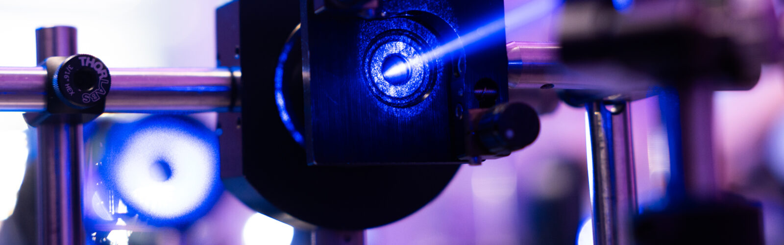 Close-up of a laser beam passing through an optical component mounted on an optical table in a photonics research laboratory.